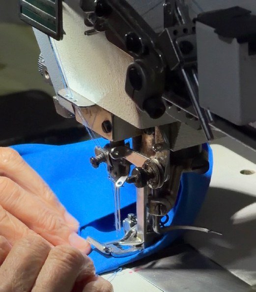 Mãos conduzindo um tecido azul na máquina de costura